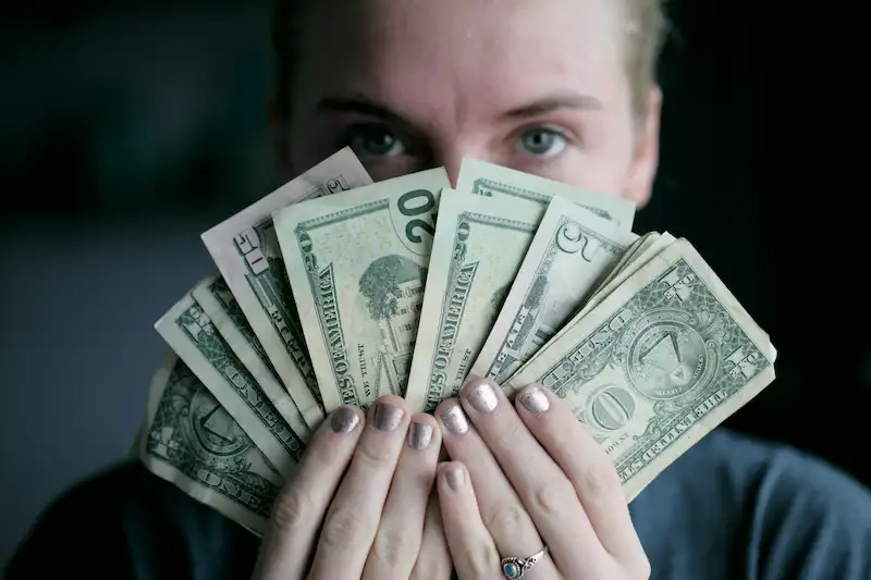 Cómo crear +5 fuentes de ingresos extra sin dejar tu empleo mujer mostrando dinero y agarrando con las manos, otras fuentes de ingresos.