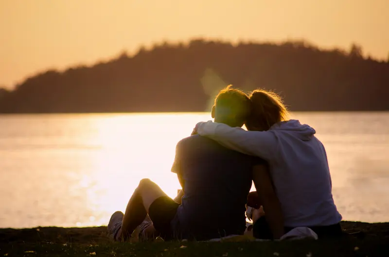 dos personas se abrazan frente a un lago en atardecer