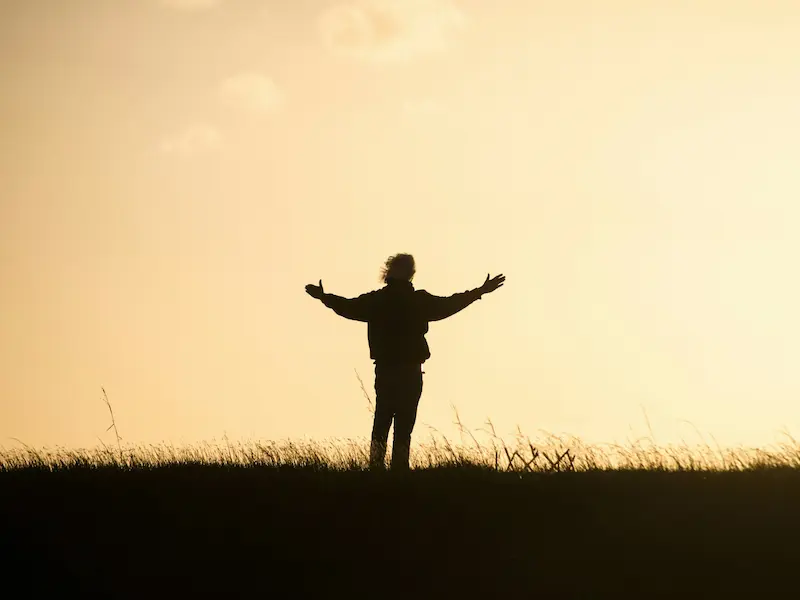 hombre agradecido levanta los brazos mirando a la puesta de sol, en terreno llano