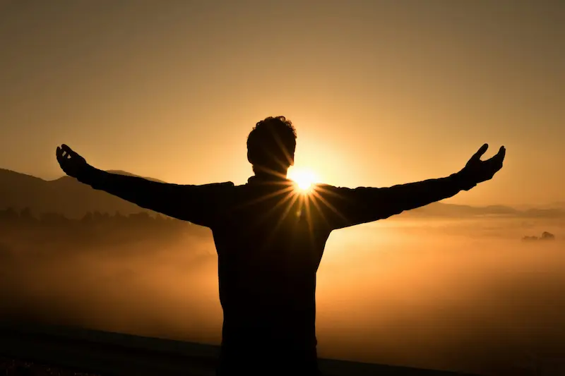 hombre feliz abriendo los brazos con una puesta de sol en frente